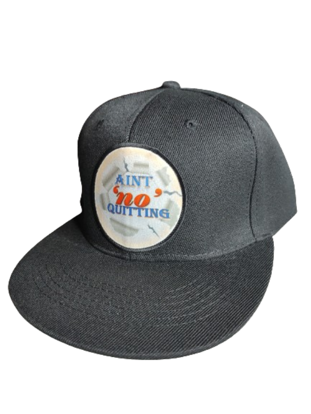 A black flat-brim baseball cap featuring a circular white patch on the front. The patch has a ripped paper effect around the edges and displays the motivational phrase "AIN'T 'NO' QUITTING" in blue and orange text. This cap is part of a never quit gift bundle, ideal for a fitness motivation gift set or empowerment apparel.
www.justsaynpromos.com