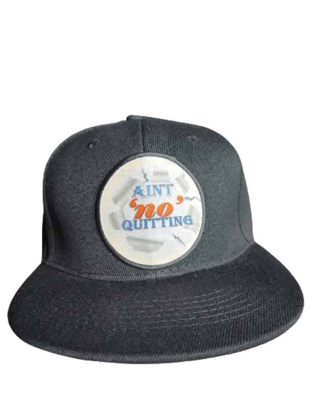 A black flat-brim baseball cap featuring a circular white patch on the front. The patch has a ripped paper effect around the edges and displays the motivational phrase "AIN'T 'NO' QUITTING" in blue and orange text. This cap is part of a never quit gift bundle, ideal for a fitness motivation gift set or empowerment apparel.
www.justsaynpromos.com